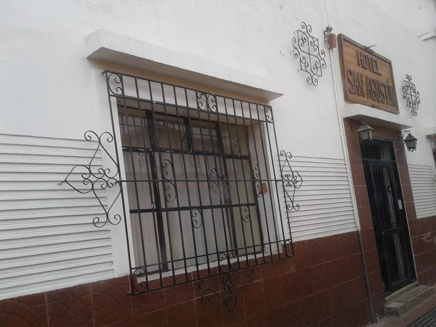 Detalle de la fachada: ventana con reja de fierro forjado, rosetón ornamental y el letrero de madera del hotel
