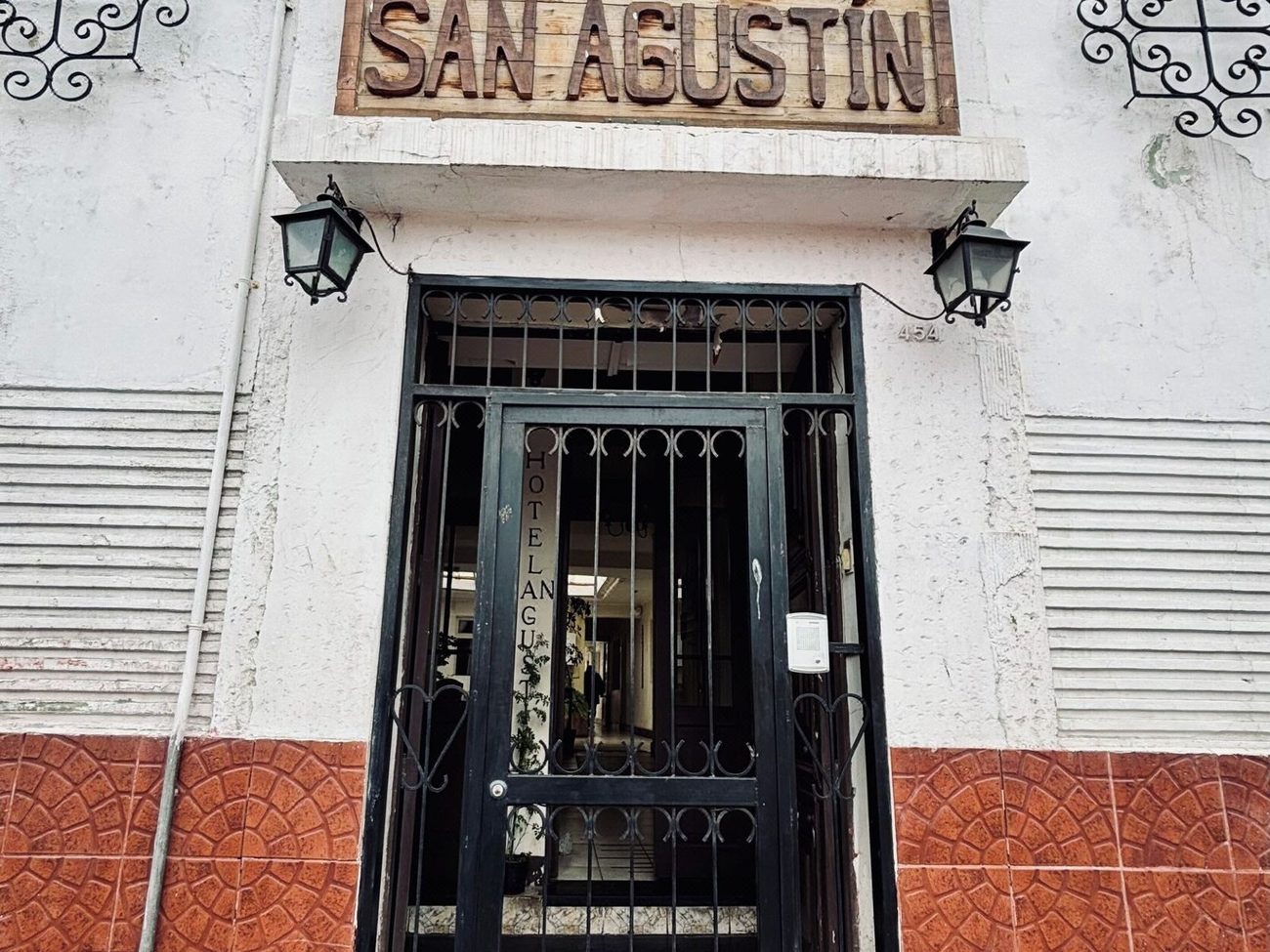 Entrada principal del hotel con su portón de fierro forjado y el letrero de madera tallada