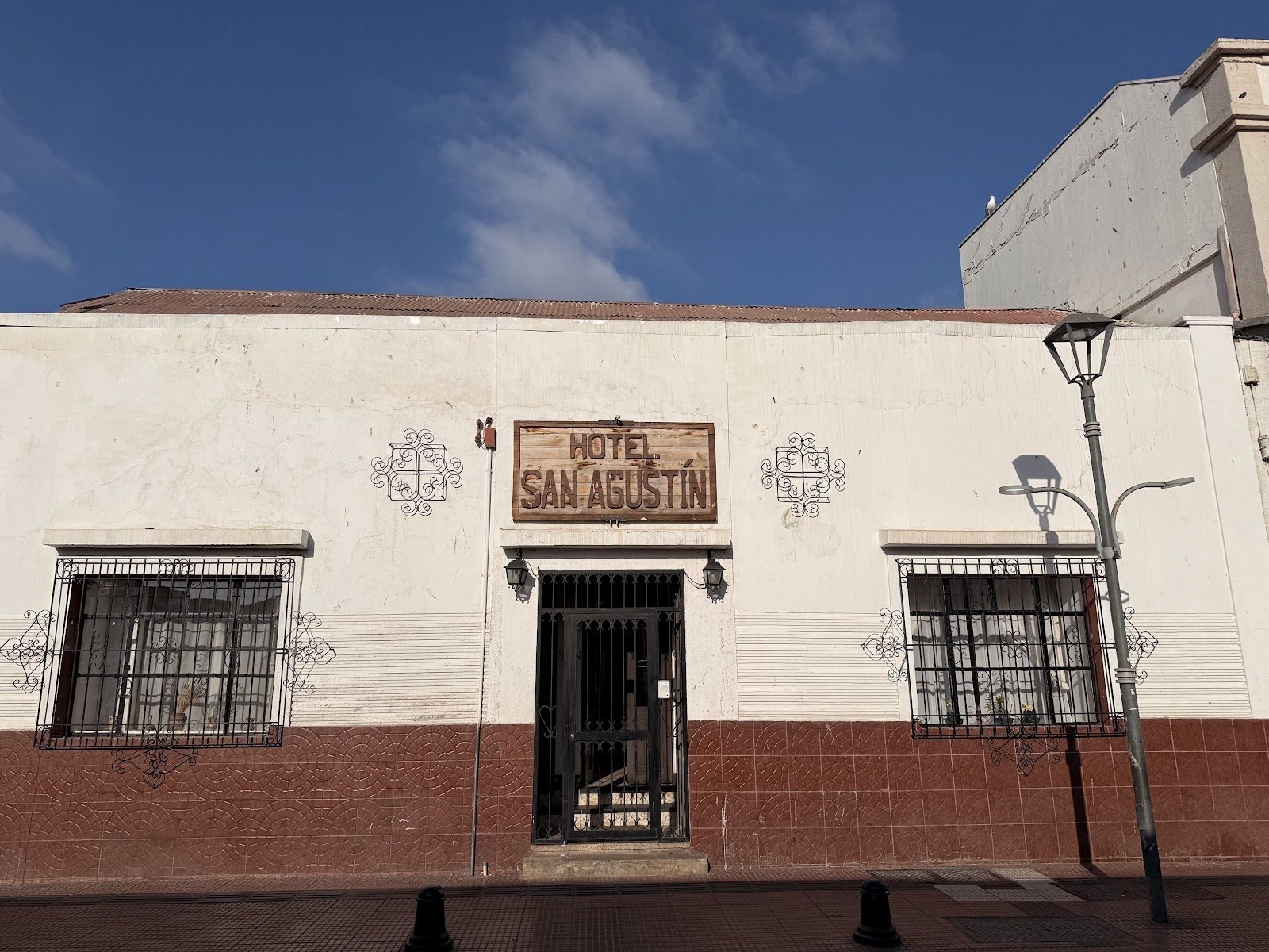 Fachada del Hotel San Agustín en Cienfuegos 454: muro encalado, zócalo de tierra, rejas de fierro forjado y el letrero de madera tallada