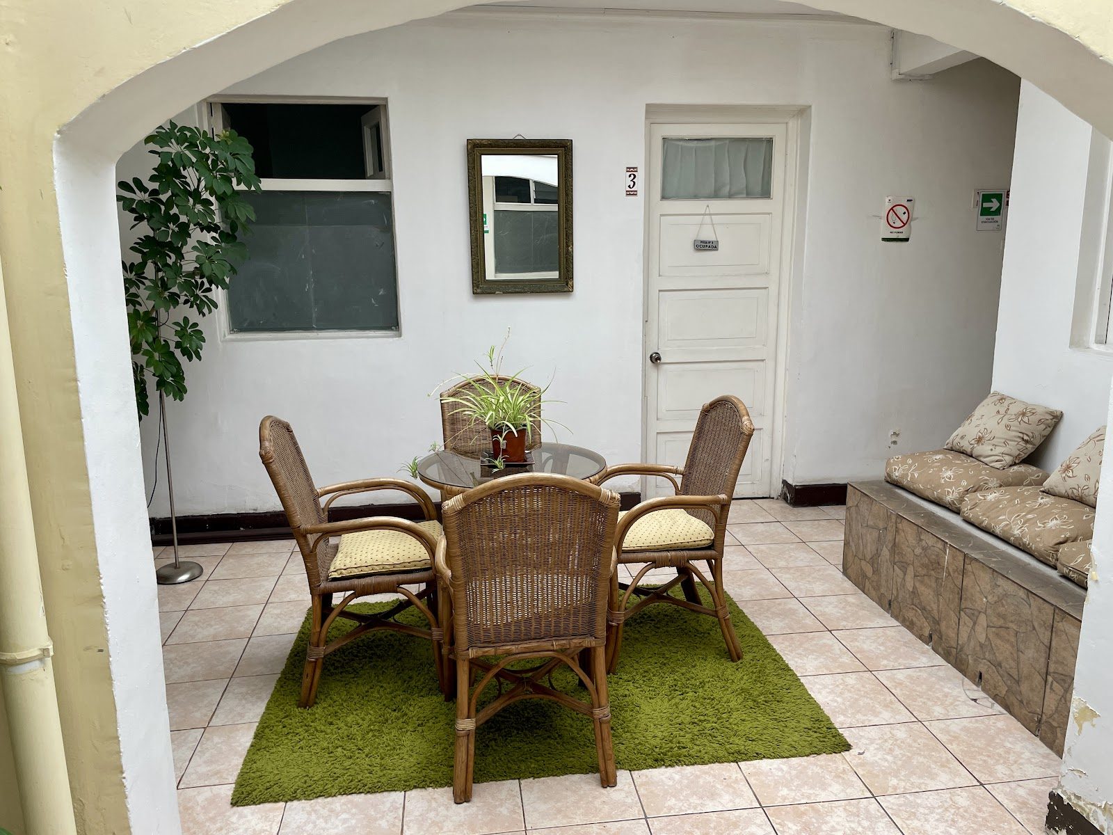 Patio interior del hotel visto bajo un arco encalado: sillones de mimbre, plantas y la puerta de una habitación